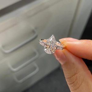 Pear-shaped three-stone engagement ring with trapezoid side stones on plain band